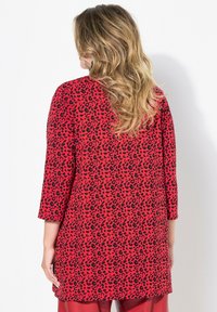 Rode tuniek met zwart luipaardprint, met een relaxte pasvorm en driekwart mouwen. Zachte stof, heuplange stijl.