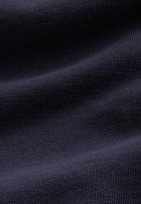 Tessuto lavorato a maglia blu navy scuro con una fine texture a coste e pieghe morbide che creano variazioni di luce e ombra.