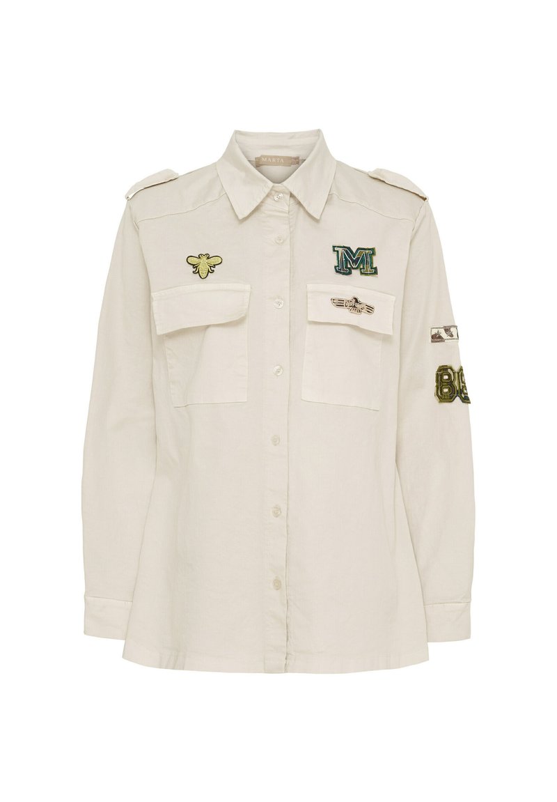 Ljust beige skjorta med knappar, axelremmar, två bröstfickor och broderade detaljer inklusive en bi och bokstaven M.