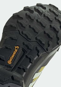 Semelle en caoutchouc noir avec des crampons profonds pour la traction, accents gris et jaunes, surface texturée, et un logo "Continental" visible.