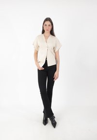 Blusa corta de manga corta en crema con escote en V profundo y cierre de botones plateados, combinada con pantalones ajustados negros y botas de tobillo negras de punta.