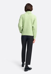 Hellgrüner, übergroßer Pullover mit hohem Kragen, geripptem Muster und seitlichen Schlitzen, kombiniert mit schwarzen, taillierten Hosen und Schuhen.