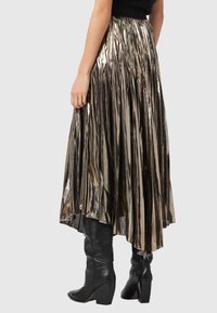 Metallic plisseret nederdel med en høj-lav kant i skinnende guld- og sølvtoner, båret med knælange sorte støvler med hæl.