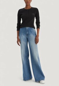 Czarna, długorękawowa koszulka henley z guzikami i logo, w połączeniu z szerokimi, jasnoniebieskimi dżinsami. Gładka tkanina i luźny krój.