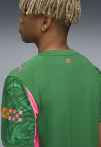 Grön sporttröja med texturerad tyg. Har rosa detaljer på ärmarna och ett grafiskt mönster. "CITY"-logotypen är placerad på baksidan.