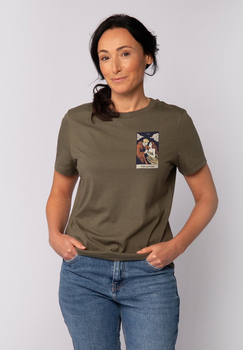 Olijfgroen katoen T-shirt met korte mouwen, met een geprinte afbeelding van twee figuren in tarotkaartstijl op de bovenste linkerborst.
