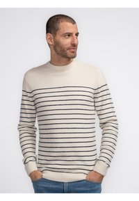 Cream-colored sweater with navy horizontal stripes, ribbed crew neck, and cuffs. Soft texture and fitted design, paired with blue jeans.