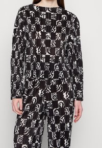Top a maniche lunghe con fantasia in bianco e nero, caratterizzato da design geometrici e astratti. Realizzato in un tessuto testurizzato con pieghe.