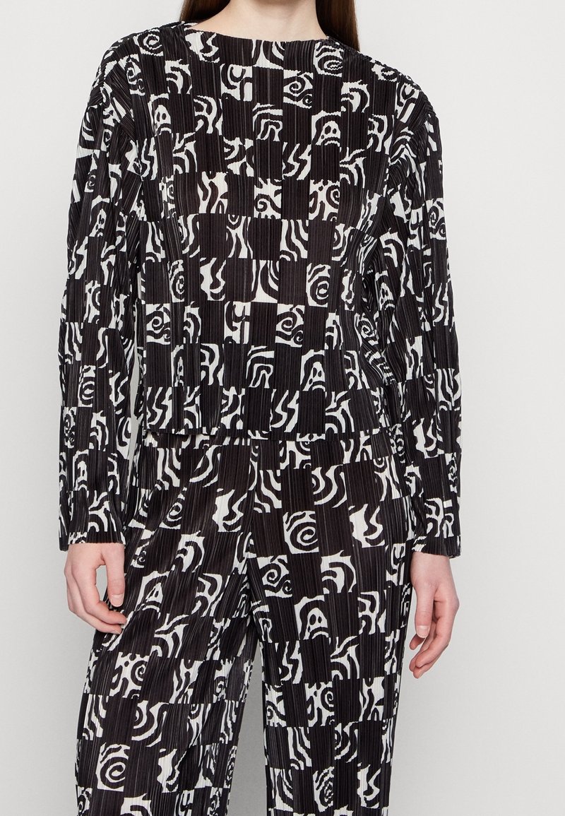 Top a maniche lunghe con fantasia in bianco e nero, caratterizzato da design geometrici e astratti. Realizzato in un tessuto testurizzato con pieghe.