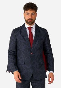 Tume sinine ülikond damaskmustriga, kahes ees taskus, punaste nuppudega ja punase aktsendiga jopel, kantud valge särgiga ja punase lipsuga.