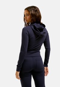 Dunkelblauer Sport-Hoodie mit taillierter Passform, weichem Material und verstellbarem Kapuzenzug. Kombiniert mit passenden, eng anliegenden Hosen mit Gesäßtaschen.
