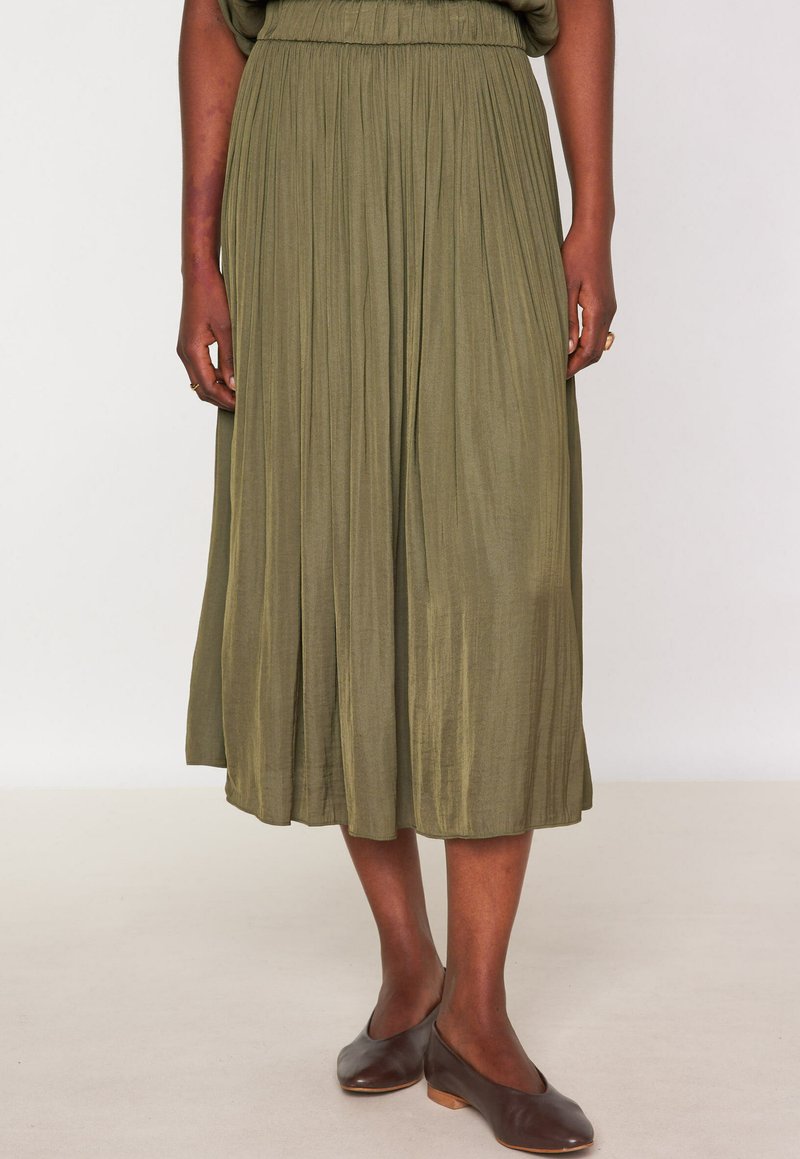 Gonna midi plissettata verde oliva con vita elastica, realizzata in tessuto leggero, abbinata a scarpe scivolate marrone scuro.