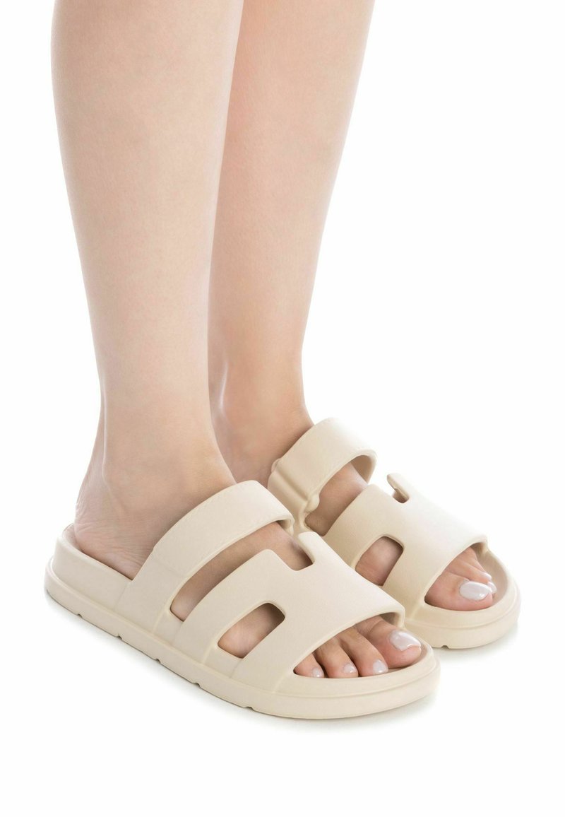 Chanclas de color beige con dos correas anchas, diseño de punta abierta y suela texturizada. Presentan detalles troquelados para mayor transpirabilidad.