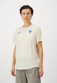 Kermakotoinen puuvillapaita, jossa on pyöreä kaula-aukko, lyhyet hihat, sininen Nike-logo ja Ranskan kansallissymbooli, joka esittää kukkoa.