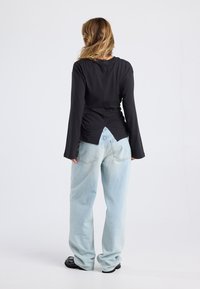 Black long-sleeve top with a gathered back detail, paired with light blue baggy jeans and black footwear, viewed from the back.