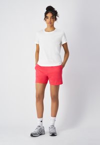 Witte kortaf t-shirt gecombineerd met roze shorts. Het model draagt grijze sneakers en witte sokken met een logo. Eenvoudig, casual ontwerp.