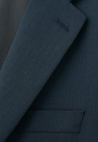 Nærbillede af revers på mørkeblå jakkesætjakke med knaphul og lomme-syning på tekstureret stof.