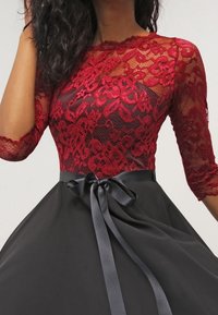 Bodice en dentelle rouge avec des motifs floraux, manches trois-quarts, et une jupe en satin noir avec un lien de taille en ruban.