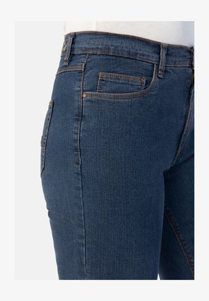 Dunkelblaue Denim-Jeans mit eng anliegendem Schnitt, ausgestattet mit orangen Nähten, Taschen und einer glatten Textur. Die Seitenansicht hebt die Form und Designdetails hervor.