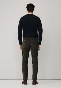 Maglione blu marina e pantaloni verde oliva con finitura testurizzata. I pantaloni presentano tasche posteriori con accenti metallici. Il modello è in posizione di spalle.