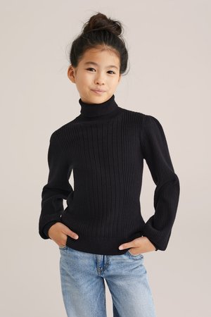 Maglione a collo alto nero a coste con maniche lunghe, caratterizzato da una vestibilità slim e un tessuto testurizzato. Abbinato a jeans in denim blu chiaro.