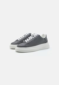 Baskets en cuir gris avec des lacets blancs et une épaisse semelle blanche. Présente un logo subtil et des détails de couture sur le dessus.