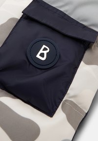 Marine-nylon mærke med en cirkulær gummiaccent, der har et hævet hvidt bogstav "B" på en stofbaggrund i camouflagemønster.
