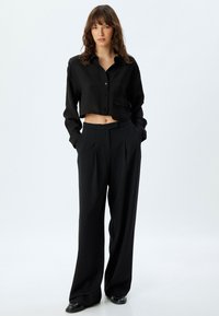Sort cropped button-up skjorte med lomme, kombineret med højlivet sorte vide bukser. Glat tekstur, minimalistisk design.