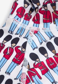 Weißer Stoff mit wiederholten Cartoon-Soldaten in roten Mänteln und blauen Hosen, mit schwarzen Pelzmützen, schwarz umrandet und mit bunten Akzenten versehen.