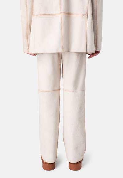 Beige textured suede jacket and pants, featuring visible seams and a relaxed fit, paired with brown-soled footwear.