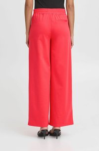 Rote weit geschnittene Hose aus strukturiertem Stoff. Verfügt über einen dehnbaren Bund und eine einzelne Gesäßtasche, kombiniert mit schwarzen Absatzsandalen.