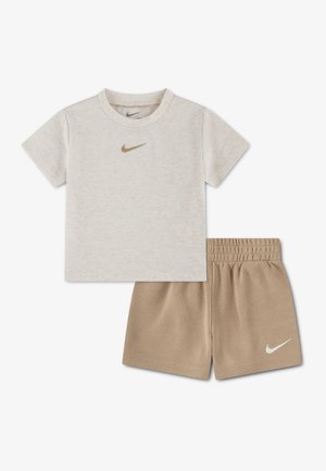 Beige short-sleeve Nike t-shirt with gold logo paired with light brown elastic waist Nike shorts with white logo on left leg.