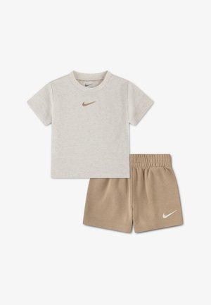 Camiseta Nike beige de manga corta con logo dorado combinada con pantalones cortos Nike marrón claro con cintura elástica y logo blanco en la pierna izquierda.