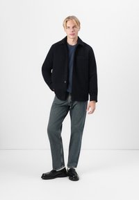 Navy button-up shirt jacket with a collar, patch pocket, paired with gray jeans and black loafers, featuring a relaxed fit and textured fabric.