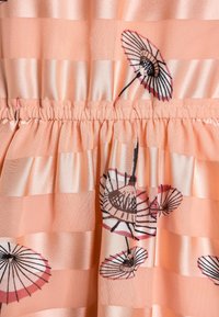 Tessuto color pesca con strisce orizzontali, caratterizzato da stampe di ombrelli floreali. Texture morbida con dettaglio in vita arricciato.