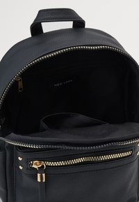 Zaino in eco-pelle nera con finitura texturizzata, dotato di una cerniera dorata, tasca frontale con cerniera e interno foderato in tessuto con etichetta.