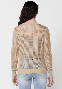 Beige, nyitott kötésű pulóver hosszú ujjakkal, rövidített fazonnal, bordázott mandzsettával és textúrázott, áttetsző hátrésszel.