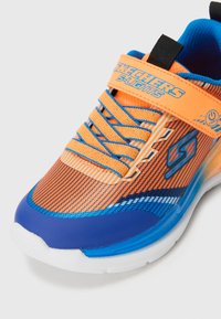 Orange and blue athletic shoe with a textured upper, featuring mesh and striped patterns, laces, and a thick white sole.