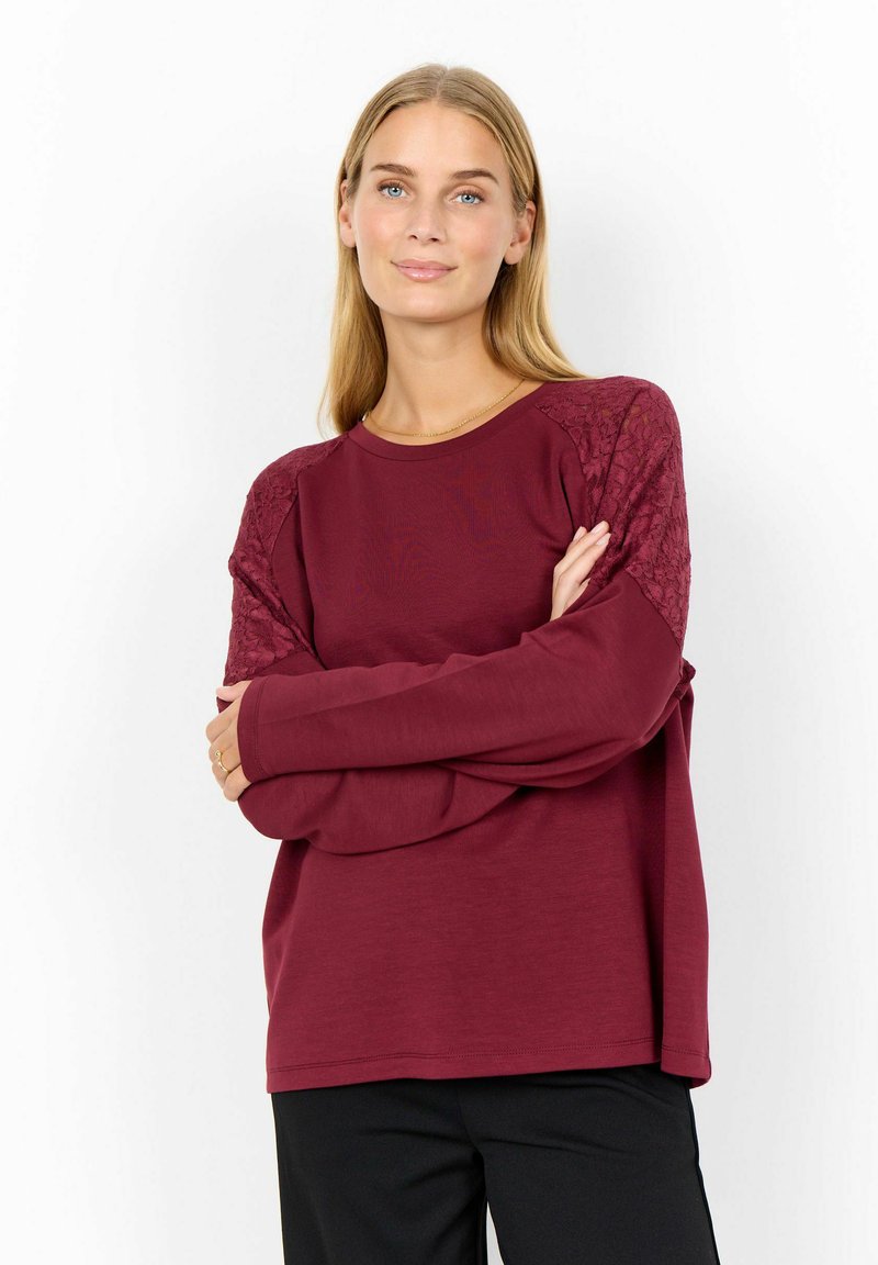 Burgundy long-sleeve sweater with textured lace accents on shoulders and a relaxed fit. Smooth fabric, crew neckline, and wide cuffs.