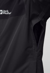 Zwarte waterdichte jas met een ritszak, voorzien van het "Jack Wolfskin"-logo en een gladde, gestructureerde stof.