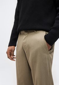 Άτομο που φορά χακί παντελόνια με το ένα χέρι στην τσέπη και μαύρο ριγέ πουλόβερ ορατό από τη μέση μέχρι το μέσο των μηρών.