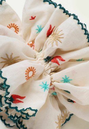 Valge riidest patsikumm rohekas-siniste laineliste servade ja mitmevärviliste päikese- ning tähekujuliste tikanditega.