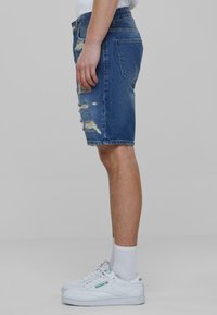 Shorts de mezclilla con detalles desgastados, con un corte clásico, color azul y cinco bolsillos, combinados con zapatillas blancas y calcetines acanalados.