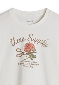 T-shirt bianca in cotone con una grafica di una rosa rosa accompagnata da foglie verdi e forbici marroni. Il testo recita "Vans Supply" in un font decorativo.