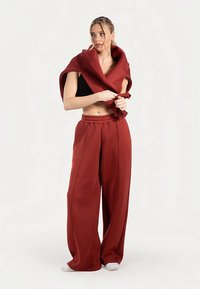 Luźne, duże bordo spodnie z teksturowanej tkaniny, z dopasowanym chustą narzuconą na ramiona, w zestawieniu z czarnym krótkim topem.