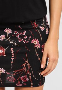 Falda negra con estampado floral que presenta flores rosas y rojas, de tela suave, diseño ajustado, y un dobladillo que se sitúa justo por encima de la rodilla.