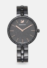 Orologio metallizzato nero con quadrante a texture scura, dettagli in oro rosa e un cinturino decorato con cristalli neri. Presenta un design a bracciale collegato.
