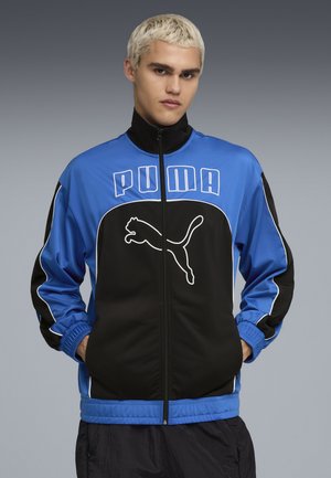 PUMA zip-jakke med en blå og sort farveskema, elastiske manchetter og et fremtrædende logo-design foran. Glat tekstur.
