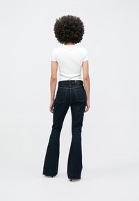 Vaqueros acampanados de mezclilla oscura con cintura alta, con detalles de costura y una cinturilla de cuero negro con marca. Combinados con una camiseta ajustada blanca.