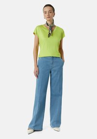 Jasnozielona bluzka z krótkim rękawem i dekoltem w serek, w połączeniu z jasnoniebieskimi, wysokim talią, szerokimi spodniami dżinsowymi. Białe buty na szpic oraz wzorzysta chustka na szyi.